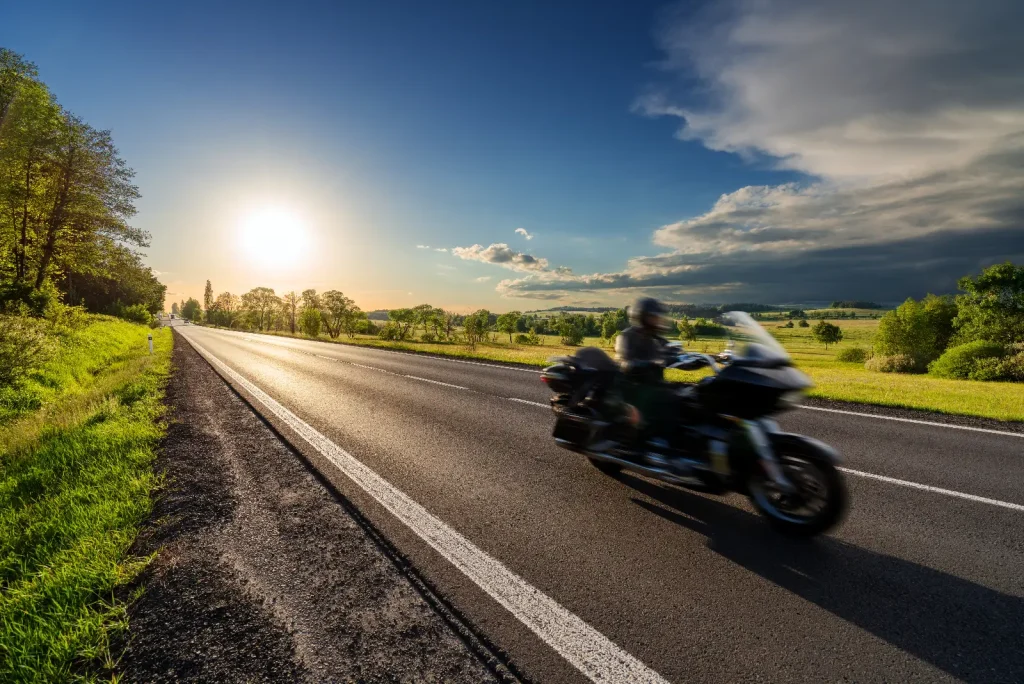 Motion blurred black motorcycle riding on an empty asphalt road in a rural landscape at sunset stock photo